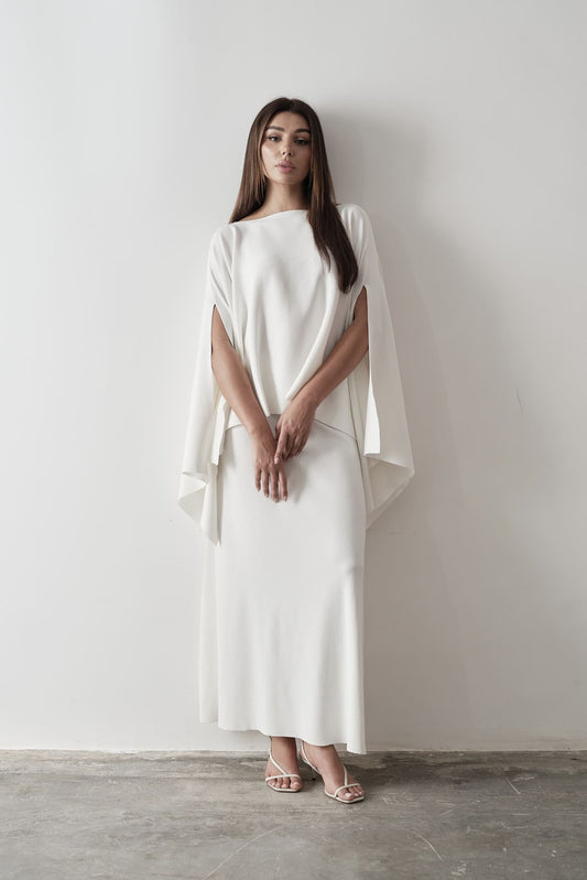Model wearing Amanda Set featuring a draped cape top and a matching floor-length skirt, styled with white strappy sandals, standing against a white background