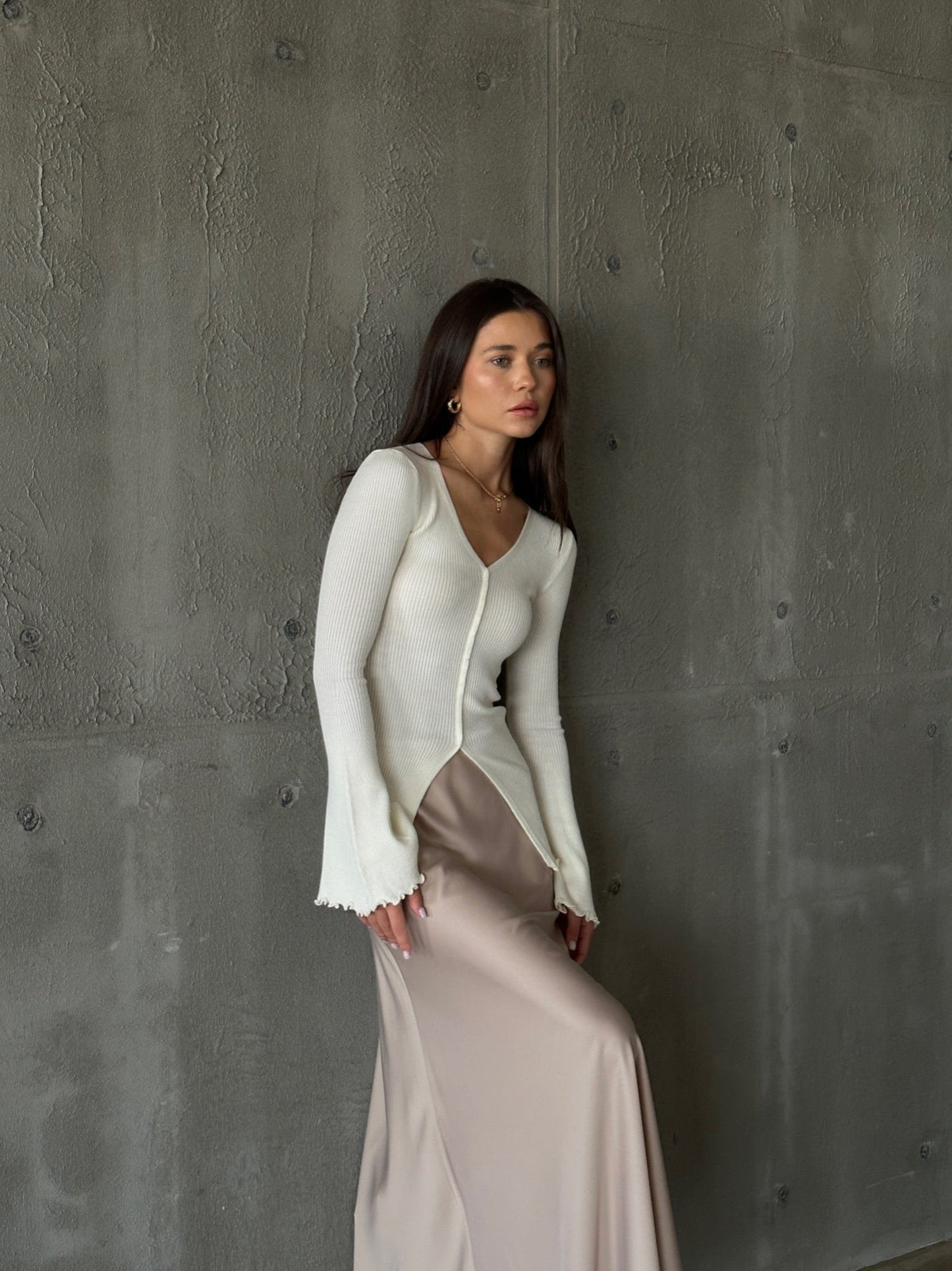 A woman models the Elara knit top, dressed in a white sweater and skirt, exuding sophistication and grace.