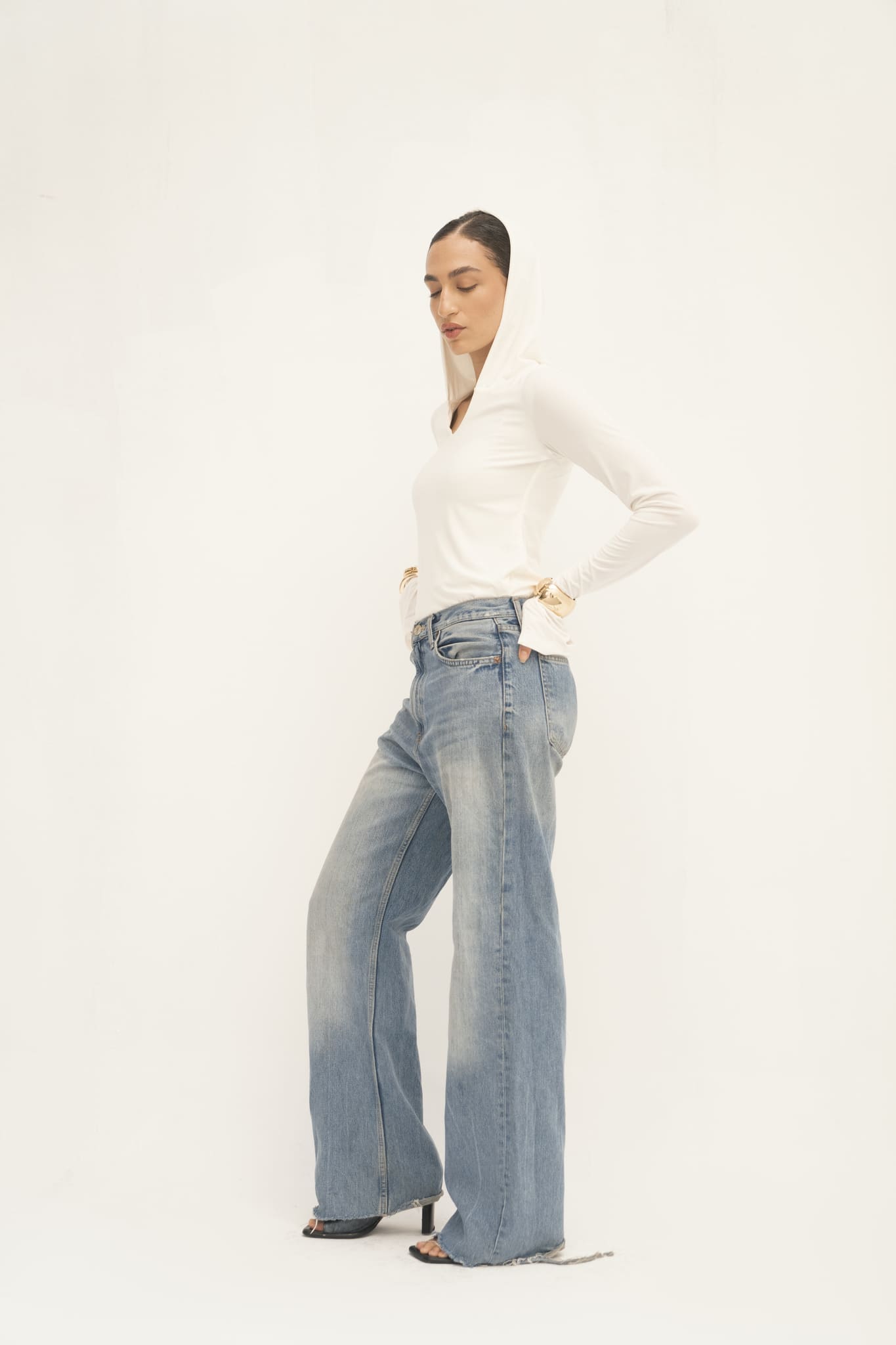 A person dressed in an Elyse Top combined with wide-leg jeans stands against a simple light backdrop, projecting a laid-back yet chic aura that effortlessly highlights its versatile functionality.